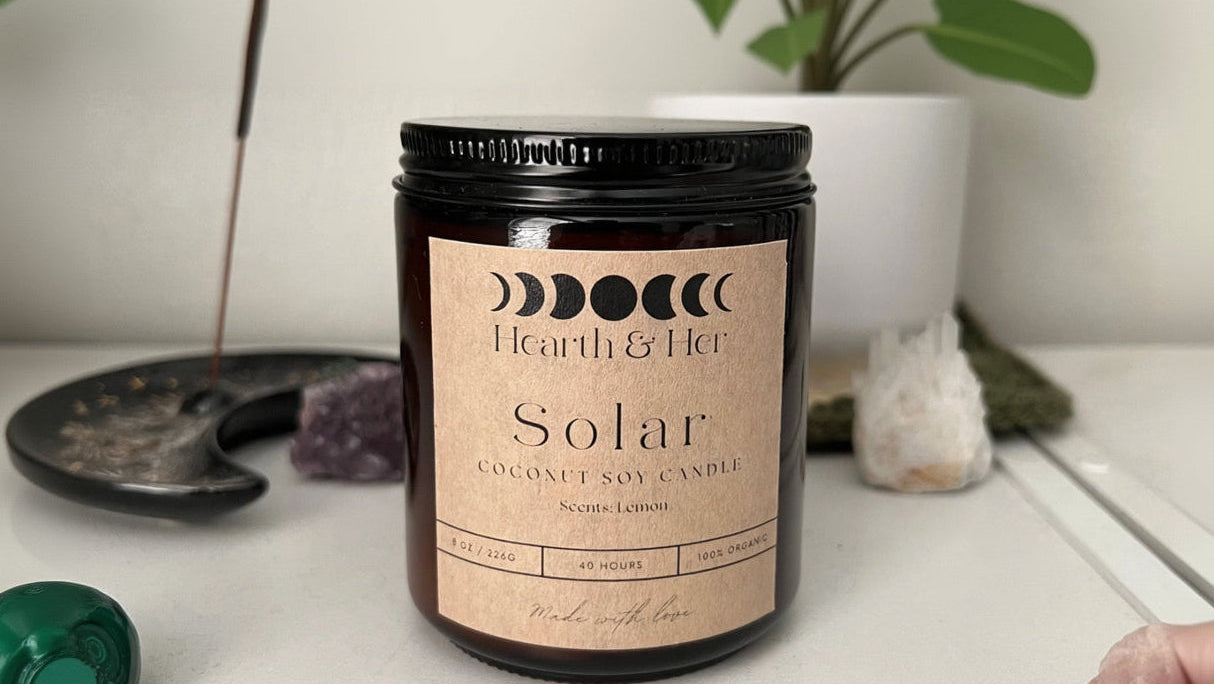 Coconut soy candle labeled 'Hearth & Her' with a plant in the background